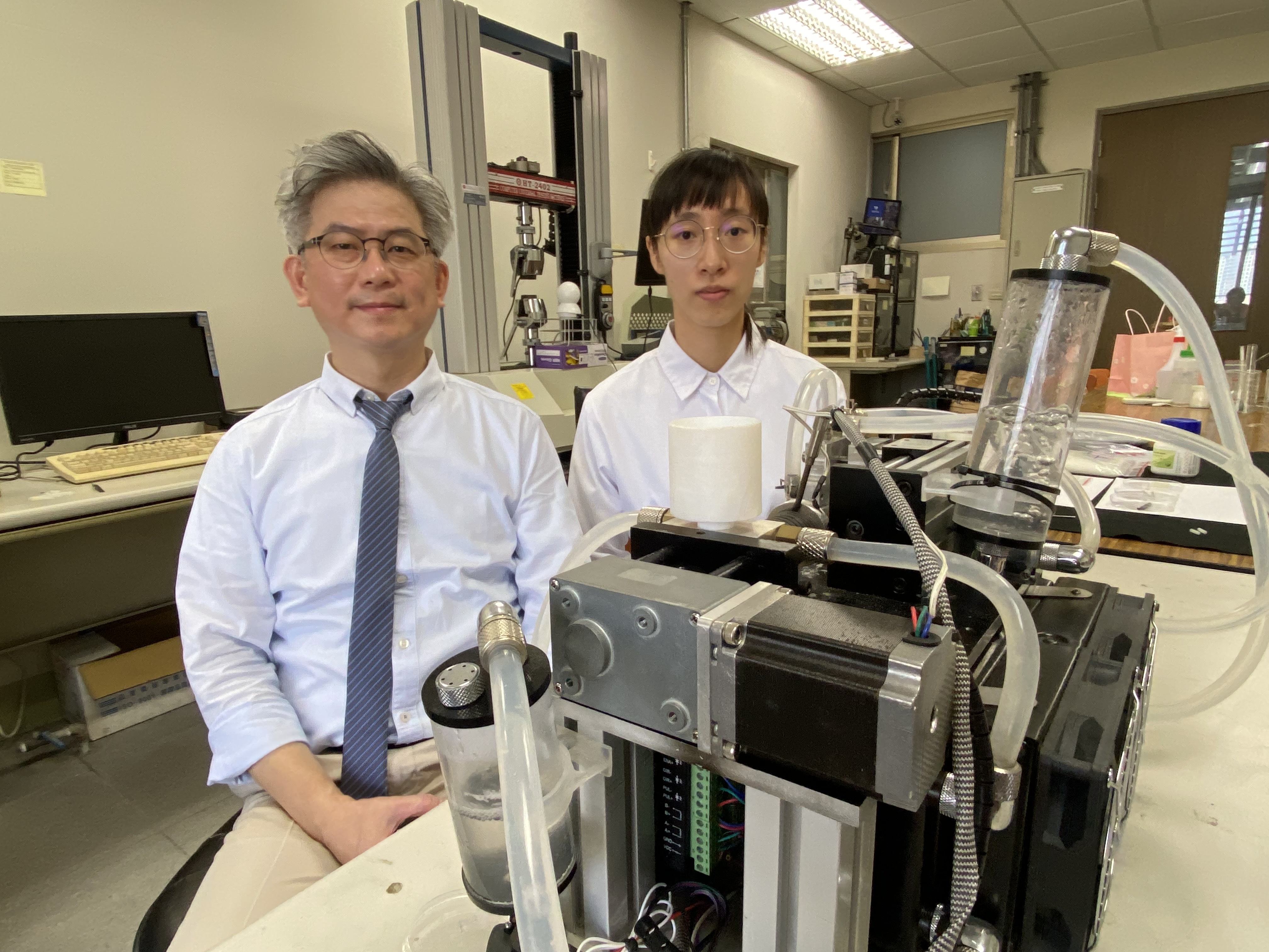 圖一：成大材料系特聘教授洪飛義（左）與博士生黃嫈庭研發血管支架全球創新材料PLAM，未來有機會嘉惠心血管疾病患者，前方為製作支架的精密微型射出機。