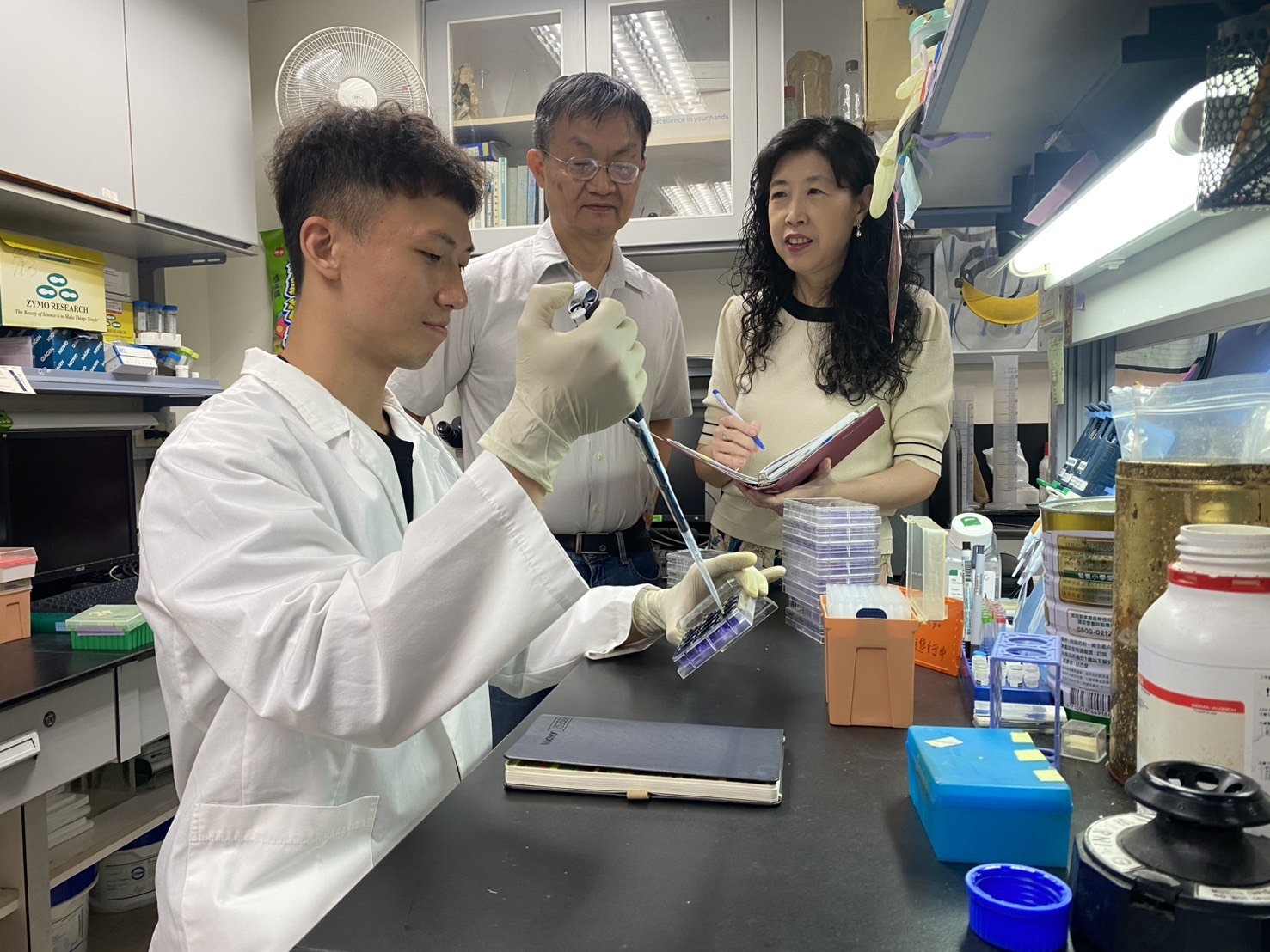 圖五:成大藥理學研究所所長王憶卿講座教授(右)與生物科技與產業科學系洪建中特聘教授(中)與博士生謝宏嘉在實驗室中的情況。